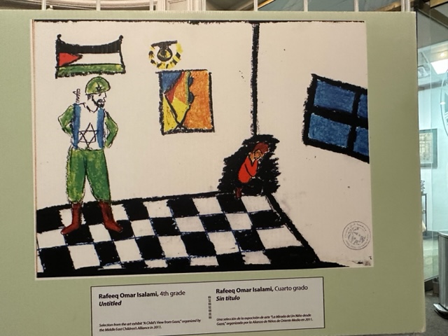 drawing by 4th-grade student of boy cowering in dark corner of room, with menacing Israeli soldier looking down at him. Palestinian flag and abstract map of israel/Palestine on wall