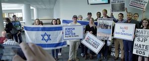 People indoors posed for group photo holding signs saying “Jewish Lives Matter—Say No to Hate”, “Know the Truth: BDS = Hate Movement”, “Say No to Anti-Semitism”, and “Hate Group: SJP Hate Movement: BDS”