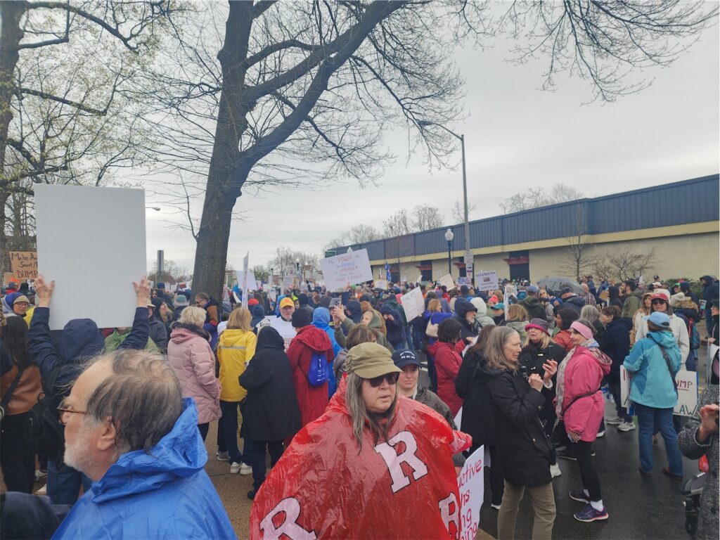 crowd of ralliers, some with signs, gathering on overcast afternoon