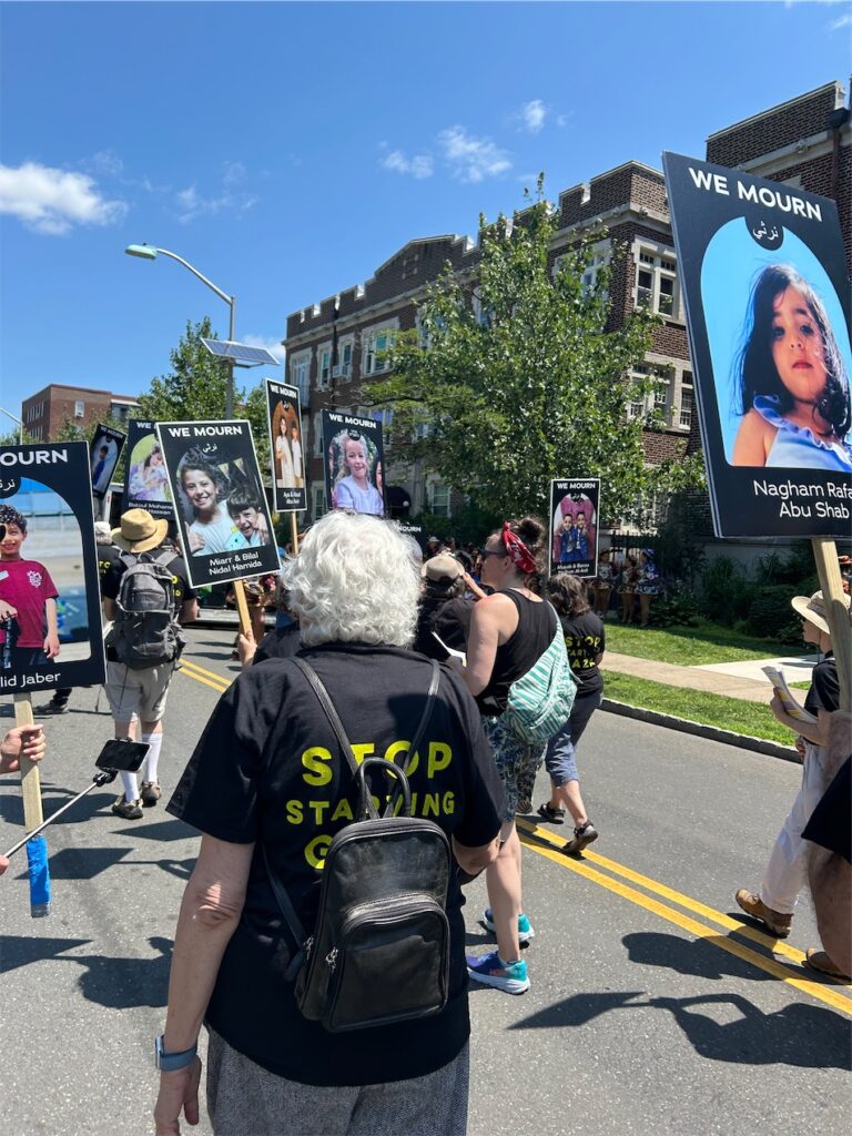 view from within parade, behind JVPers in “Jews Say Let Gaza Live” T-shirts and others holding signs of children, Palestinian and Israel, killed in war.