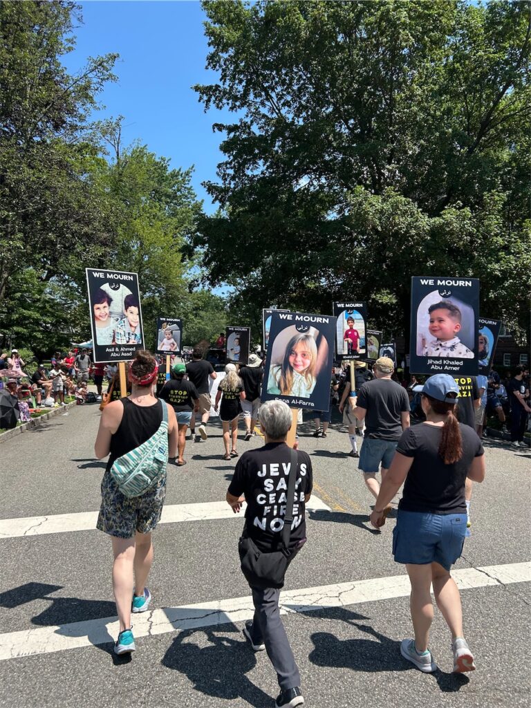 view from within parade, behind JVPers in “Jews Say Let Gaza Live” T-shirts and others holding signs of children, Palestinian and Israel, killed in war.