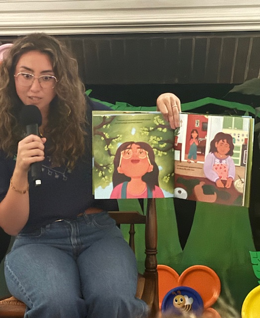 Author Jenan A. Matari speaks into a microphone while holding open a page from her book “Everything Grows in Jiddo’s Garden”