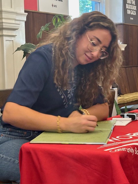 Author Jenan A. Matari signs a copy of her book on a table covered by a Words Community Bookstore tablecloth