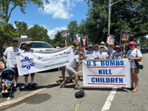 JVP members stand with banners reading “U.S. BOMBS KILL CHILDREN” and “Jewish Voice for Peace Northern New Jersey, jvpnorthjersey.org” some carry signs with photos of dead Palestinian or Israeli children; most wear white T-shirts saying “Jews Say Fund People not Bombs”